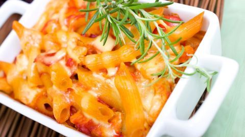 Ein Nudelauflauf mit Hackfleisch und Paprika ist in einer weißen Auflaufform zu sehen, überbacken mit Käse und frischen Kräutern.