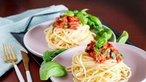 Spaghetti mit frischer Basilikumsoße und Tomaten wird appetitlich auf rosa Tellern serviert, umgeben von Basilikumblättern.
