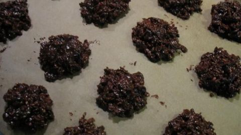 Dunkle, grobe Kekse liegen auf einem Backblech mit Backpapier, im Abstand zueinander, bereit für den Backofen.