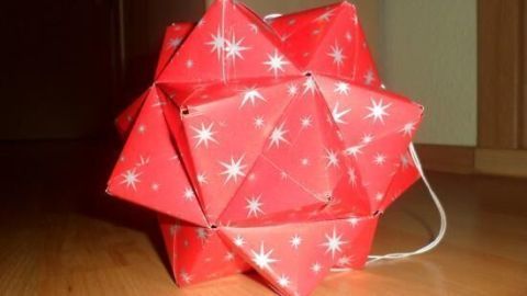 Ein roter Kartonstern aus Geschenkpapier liegt auf dem Boden und wirkt festlich mit schimmernden Sternen auf der Oberfläche.