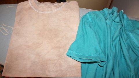 Eine beiges T-Shirt und eine türkisfarbene Bluse liegen nebeneinander auf einem Bügeltisch, bereit zum Bügeln ohne Bügeleisen.
