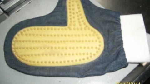 Ein Noppenhandschuh liegt auf einer Oberfläche und ist bereit, Hundehaare zu entfernen. Der Handschuh hat eine gelbe, strukturierte Oberfläche.