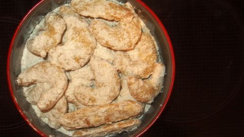 Dinkel-Vanillekipferl liegen gebacken in einer roten Schüssel und sind mit Puderzucker bestäubt, bereit zum Servieren.