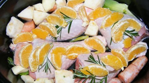Saftige Putenoberkeule mit Orangenstücken und Rosmarin liegt auf einer bunten Gemüsemischung in einer Schüssel.