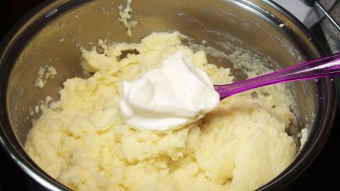Eine Schüssel mit Kartoffelpüree, in die ein Löffel Frischkäse gegeben wird, um es zu verfeinern.