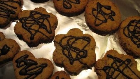 Plätzchen mit verschiedenen Keksausstechern sind auf einem glänzenden Blech angeordnet und mit dunkler Schokolade verziert.