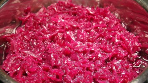 Apfelrotkohl wird in einem Topf zubereitet und zeigt eine glänzende, tiefrote Farbe, umgeben von einer Küchenumgebung.