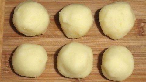 Sechs glatte, rohe Kartoffelklöße liegen auf einem Holzbrett und warten darauf, in einem Gericht verwendet zu werden.