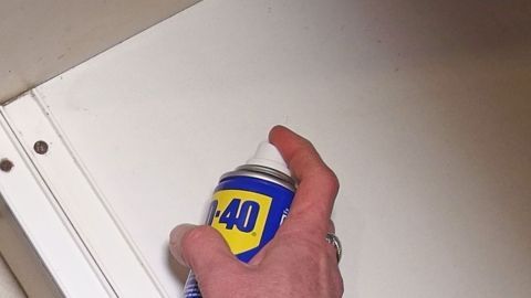 Eine Hand hält eine Spraydose, um fettige Küchenregale zu reinigen, während sie in einer hellen Küchenschrankfläche wirkt.