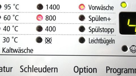 Eine Waschmaschinenbedienung zeigt Temperatur- und Schleudereinstellungen, während umweltfreundliches Waschmittel hergestellt wird.