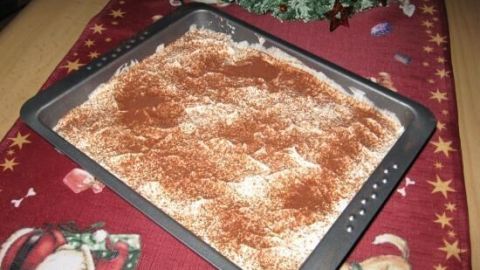 Ein Tiramisu auf einem Blech, bestreut mit Kakaopulver, liegt auf einem festlichen, weihnachtlich dekorierten Tisch.