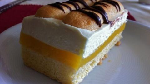 Ein Orangen-Biskuit liegt auf einem weißen Teller, mit sahniger Creme und einer Schicht orangefarbener Füllung.