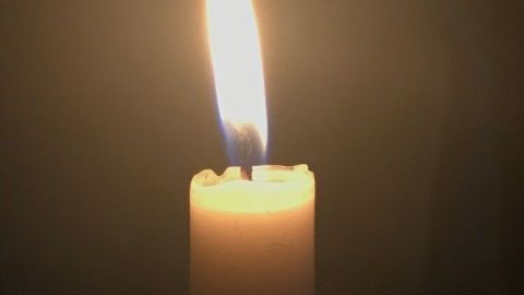Eine brennende Kerze steht in einem Halter, während die Flamme sanft im Dunkeln leuchtet, ohne zu spritzen.