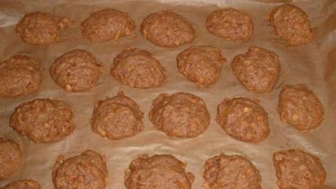 Bratapfelkekse liegen in Reihen auf einem Backblech mit Backpapier. Sie sind gleichmäßig verteilt und goldbraun gebacken.