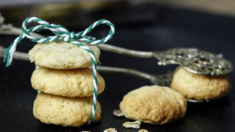 Drei kernige Haferflocken-Plätzchen sind auf einem dunklen Tisch gestapelt und mit einer grünen Schnur gebunden, umgeben von Haferflocken.