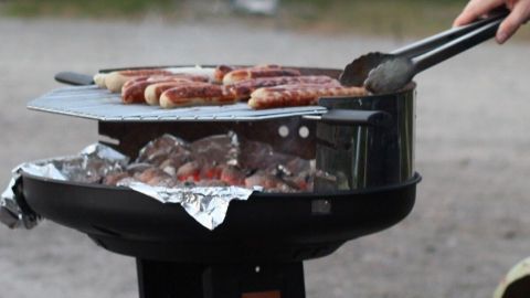 Ein Grill mit frischem Fleisch auf dem Rost wird zubereitet, während ein Mensch mit einer Zange darauf herumgrillt.