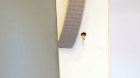 Ein grauer Griff hängt locker am Schrank und berührt einen kleinen Holzstift in einem Loch der Schranktür.