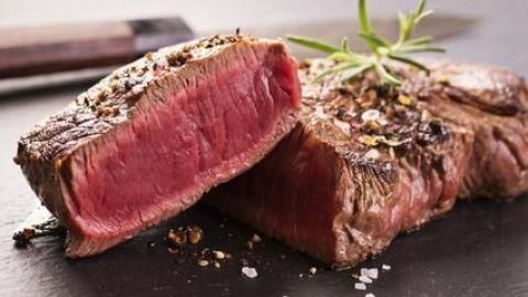 Rumpsteaks liegen auf einem schwarzen Untergrund, eines ist halbiert und zeigt rosafarbenes Fleisch, garniert mit Gewürzen und Rosmarin.