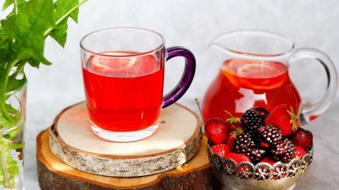 Ein Glas fruchtiger Durstlöscher steht auf einem Holzuntersetzer, während ein Krug neben frischen Beeren platziert ist.