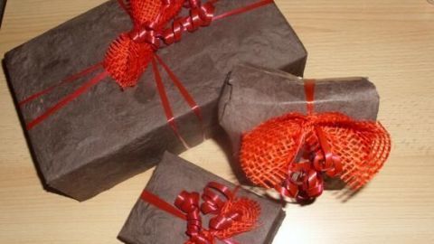 Schöne, preiswert verpackte Geschenke in verschiedenen Größen liegen auf einem Tisch und sind mit rotem Dekoband verziert.