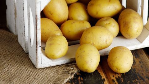 Kartoffeln halten deutlich länger und keimen viel seltener, mithilfe dieser Kartoffelkiste aus Holz. Eine kleine Holzkiste mit gelben Kartoffeln steht auf einer Holzoberfläche, umgeben von einem Jutesack.