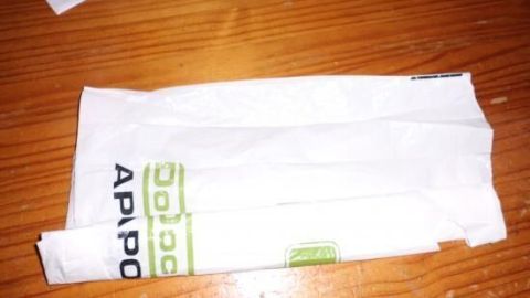 Eine weiße Plastiktüte wird auf einem Holztisch sorgfältig gefaltet. Auf der Tüte steht "APO".