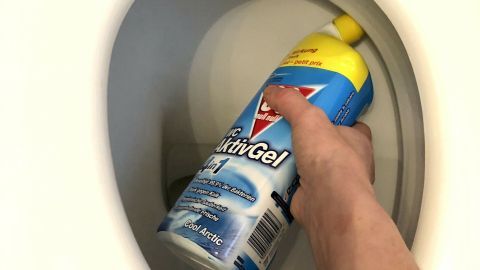 Eine Hand hält eine Flasche mit Toilettenreiniger über das Toilettenbecken zum Reinigen der Oberfläche.