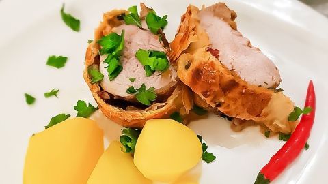 Zartes Schweinefilet im Blätterteig, garniert mit frischer Petersilie, dazu Kartoffeln und eine Chili-Schote.