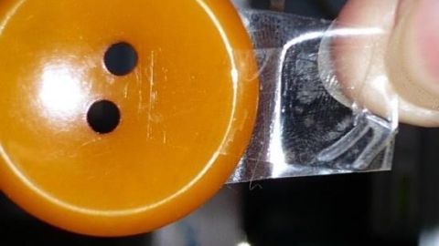 Ein orangefarbener Knopf wird an ein Stück Klebeband gehalten, vermutlich als Schritt in einem Bastelprojekt zum Thema Schnurrer.