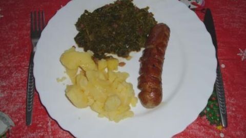 Ein Teller mit gebratenem Grünkohl, einer Bratwurst und Kartoffeln, serviert auf einem festlichen Tisch.