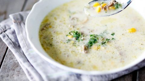 In einer weißen Schüssel wird eine cremige Lauch-Creme-Suppe serviert, während ein Löffel sie behutsam umrührt.