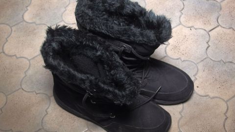 Schwarze Winterstiefel mit kuscheligem Fellrand stehen auf einem Steinboden, bereit für kalte Tage im Auto.