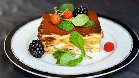 Ein köstliches Tiramisu mit Eierlikör und Vanillepudding liegt auf einem Teller, umgeben von frischen Beeren und Minze.
