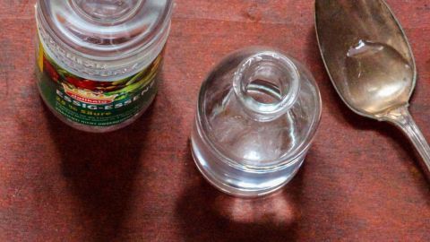 Eine Flasche Essig und ein kleines Glas stehen neben einem Löffel auf einem Holzuntergrund, bereit zum Gurgeln gegen Halsschmerzen.