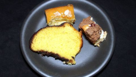 Ein Stück gelber Kuchen und zwei kleine Stücke Schokoladenkuchen liegen auf einem schwarzen Teller und warten auf Genuss.