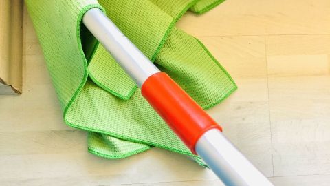 Ecken am Boden ohne Mühe reinigen, mit diesem kleinen Tipp: Da bei mir diverse Gelenke (hauptsächlich Knie und Handgelenk) für Hausarbeit streiken, habe ich das Problem so gelöst. Ein grünes Tuch ist an einem Besenstiel befestigt, bereit zum Reinigen von Bodenecken in einem hellen Innenraum.