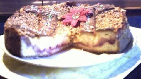 Ein Apfel-Zimtkuchen steht auf einem Teller, eine Scheibe fehlt. Eine rote Blume schmückt die knusprige Kruste.