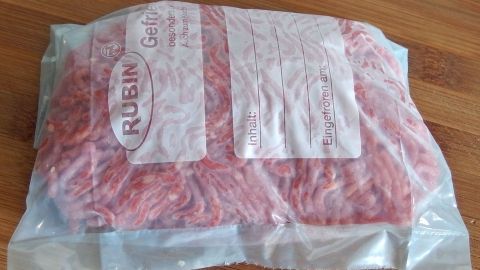 Ein gefrorenes Paket Hackfleisch liegt auf einer Holzoberfläche, bereit zum Einlagern oder Zubereiten.