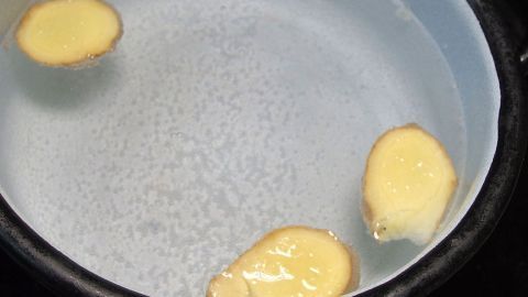 Drei ingwerartige Stücke schwimmen in klarem Wasser in einem Kochtopf und ziehen Geschmack für ein gesundes Getränk.