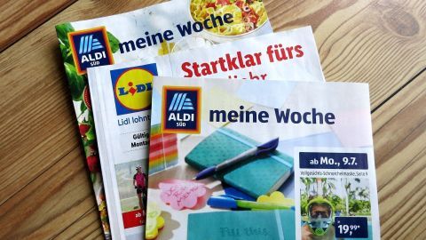 Prospekte von Aldi Süd und Lidl liegen auf einem Holztisch. Auf dem Aldi-Prospekt steht "meine Woche" und "ab Mo., 9.7".