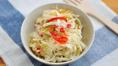 Ein Schüsselchen mit frischem Krautsalat, garniert mit Paprika, steht auf einem gestreiften Stoffuntergrund.
