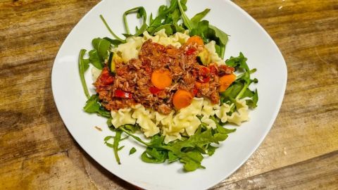 Pasta mit Thunfisch liegt auf einem Bett aus frischem Rucola, umgeben von einem rustikalen Holztisch.