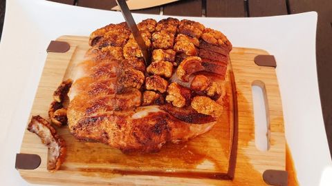 Ein saftiger Krustenbraten liegt auf einem Holzbrett und wird mit einem Messer geschnitten, um ihn zu servieren.