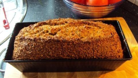 Frisches Low Carb Brot liegt in einer schwarzen Form auf einem Holzbrett, während im Hintergrund rote Tomaten in einer Schüssel stehen.