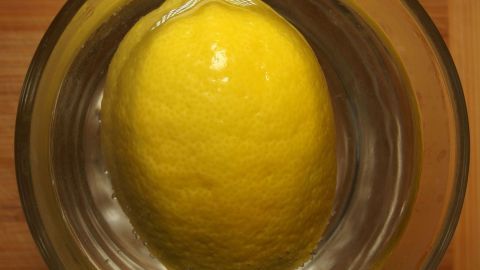 Um mehr Saft aus einer Zitrone zu gewinnen, lege sie vor dem Auspressen in heißes Wasser. Dieser einfache Trick wird den Saftfluss maximieren und erleichtert das Auspressen. Perfekt für die nächste Limonade oder zum Kochen. Zitrone schwimmt in klarem Wasser in einem Glas mit Holztisch als Hintergrund. Kein Text vorhanden.
