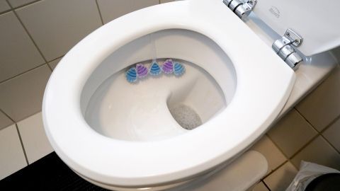 Eine saubere WC-Schüssel mit drei bunten WC-Steinen hängt am Rand; gefliester Boden und Badezimmerumgebung.