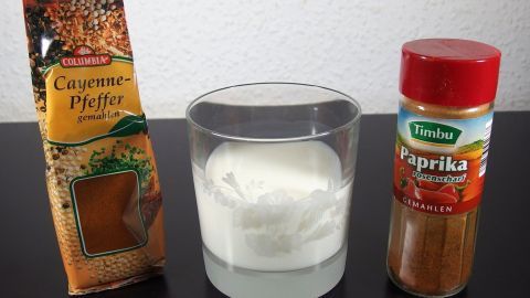 Eine Glas mit Milch steht zwischen zwei Gewürzpackungen, einer für Cayennepfeffer und einer für Paprika, die scharfes Essen mildert.