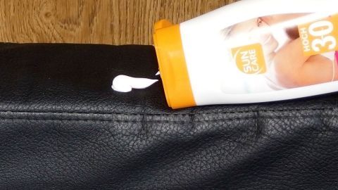 Eine Flasche Sonnencreme steht über einer Ledercouch, während ein Klecks der Creme auf das Leder gedrückt wird.
