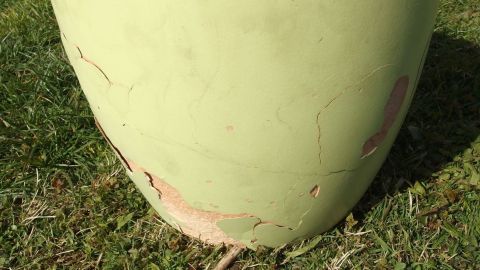Ein Pflanzgefäß aus Ton steht auf grünem Gras und zeigt Risse, die durch Frost entstanden sind.