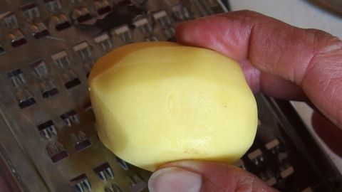 Eine geschälte Kartoffel wird auf einer Reibe bearbeitet, um geriebene Kartoffel zur Behandlung von Augenringen herzustellen.